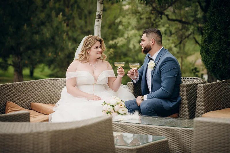 Свадьба на природе, жених и невеста пьют шампанское в беседке