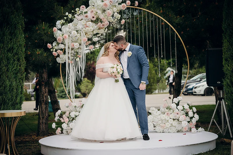 Жених и невеста целуются на арке украшенной цветами